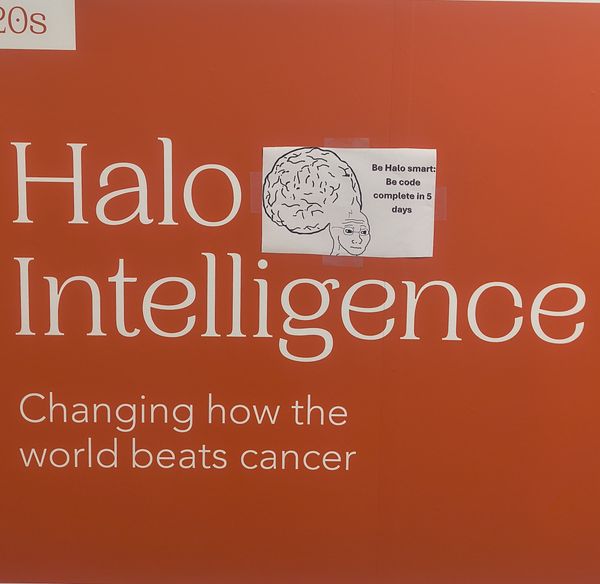The image features a bright orange background with the text "Halo Intelligence" prominently displayed in white. Below, it states, "Changing how the world beats cancer." A small white sticker with a brain illustration and the text "Be Halo smart: Be code complete in 5 days" is affixed to the orange surface.
