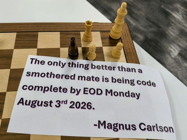 The image features a chessboard with a few pieces, including a black pawn and white rook, placed on a wooden board. A white paper with a black border and purple text reads, "The only thing better than a smothered mate is being code complete by EOD Monday August 3rd 2026." The quote is attributed to Magnus Carlson. The setting appears to be indoors, with a dark, textured surface in the background.