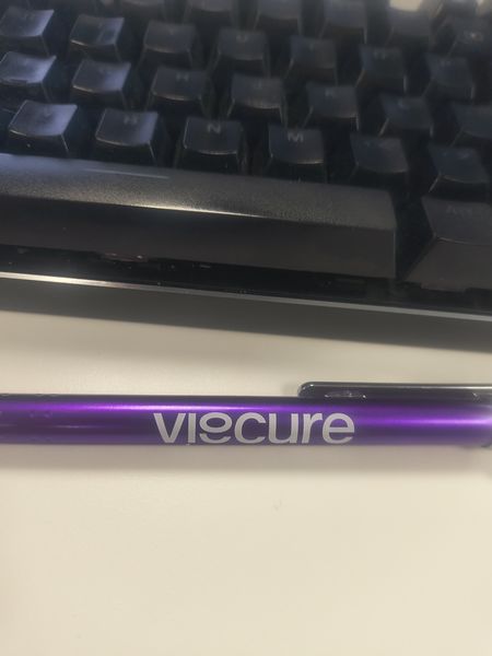 The image shows a close-up of a black keyboard with visible keys and a purple pen labeled "VIECURE" resting on a white surface.