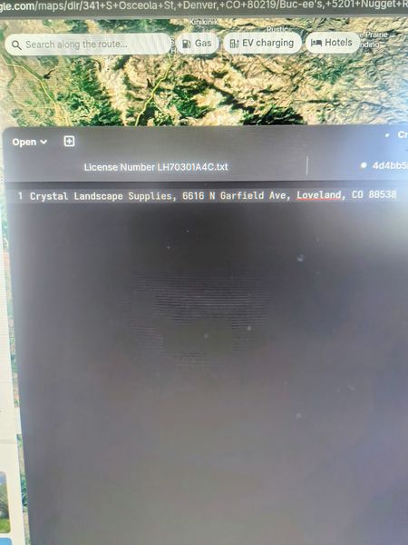 The image shows a computer screen displaying a Google Maps interface with a satellite view of a mountainous area. Below the map, a text box lists "Crystal Landscape Supplies, 6616 N Garfield Ave, Loveland, CO 80538," indicating a business location. The screen also shows a partially visible text file with a license number and a file path.
